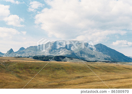 Mountain range rises above a valley against a blue sky Mountain range rises above a valley against a blue sky 86380970