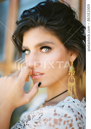 Young girl in a white wicker dress touches her chin with her fingers. Portrait 86381009