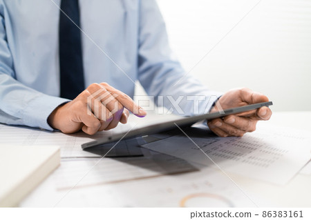 Working Man Conept The male employee sitting at his desk, holding a tablet, and touching the screen of his work 86383161