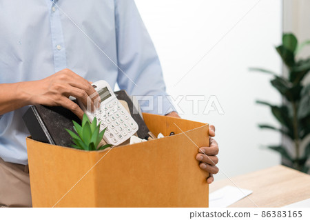 Resignation Concept The man in light blue shirt standing at the desk and putting the calculator and other stuff into the box Resignation Concept The man in light blue shirt standing at the desk and putting the calculator and other stuff into the box 86383165