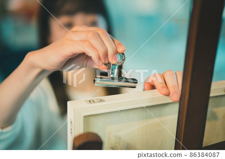 A woman's hand drawing by fixing the drawing paper to the B3 panel with the eyeball clip A woman's hand drawing by fixing the drawing paper to the B3 panel with the eyeball clip 86384087