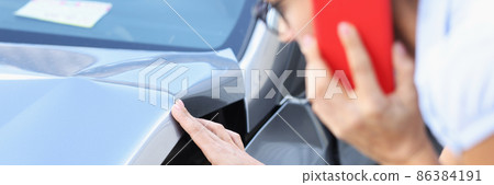 Woman driver is talking on smartphone and examines damage to car after accident closeup Woman driver is talking on smartphone and examines damage to car after accident closeup 86384191
