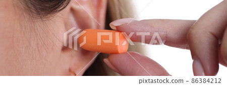 Woman inserts orange earplugs into ears closeup Woman inserts orange earplugs into ears closeup 86384212