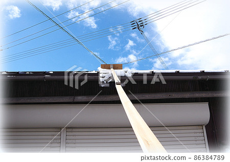 [HDR style] A scene where the snow on the roof is being removed with a homemade snow-stripping tool with a blade attached to the tip of a long rod. 86384789