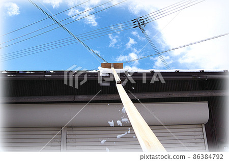 [HDR style] A scene where the snow on the roof is being removed with a homemade snow-stripping tool with a blade attached to the tip of a long rod. 86384792