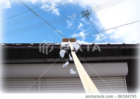 [HDR style] A scene where the snow on the roof is being removed with a homemade snow-stripping tool with a blade attached to the tip of a long rod. 86384795