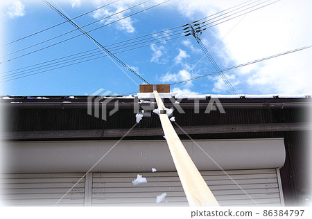 [HDR style] A scene where the snow on the roof is being removed with a homemade snow-stripping tool with a blade attached to the tip of a long rod. 86384797