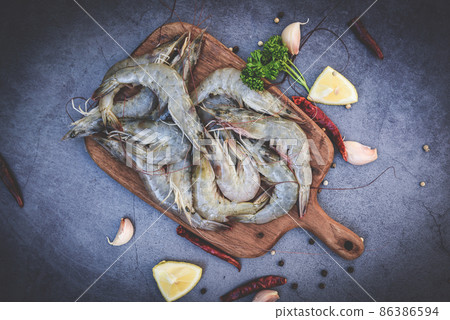 raw shrimps on wooden cutting board plate, fresh shrimp prawns for cooking with spices lemon garlic black pepper chili on dark background in the seafood restaurant, top view raw shrimps on wooden cutting board plate, fresh shrimp prawns for cooking with spices lemon garlic black pepper chili on dark background in the seafood restaurant, top view 86386594