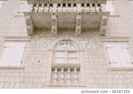 White building with stone balcony, arched windows and shutters 86387388