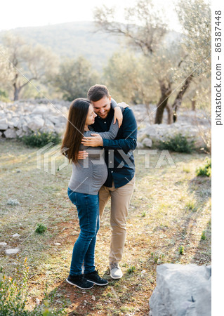 Man hugging pregnant woman in park 86387448
