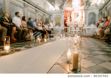 Candles in glasses burn along the white carpet in the temple during the wedding ceremony Candles in glasses burn along the white carpet in the temple during the wedding ceremony 86387492