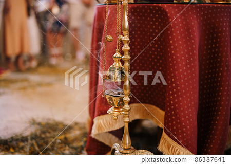 Smoking censer hangs on a gold stand in a temple near a table with a red tablecloth 86387641