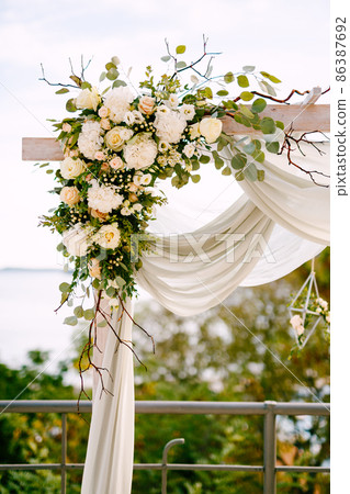 Fragment of a wedding arch decorated with tea roses, green leaves, branches and white cloth Fragment of a wedding arch decorated with tea roses, green leaves, branches and white cloth 86387692