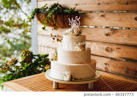 White three-tiered wedding cake with flowers on a wooden table White three-tiered wedding cake with flowers on a wooden table 86387773