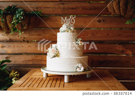 Three-tiered wedding cake stands on a stand with legs on a wooden table 86387814