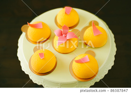 Individual yellow mousse cakes decorated with glazed flowers on an icing turntable Individual yellow mousse cakes decorated with glazed flowers on an icing turntable 86387847