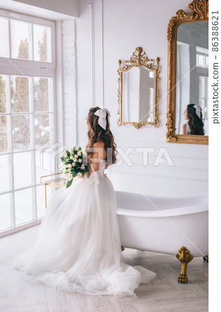 Beautiful bride with bouquet in wedding dress sitting in studio. Bride view from the back 86388621