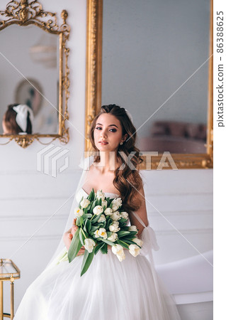 Beautiful bride with bouquet in wedding dress sitting in studio 86388625
