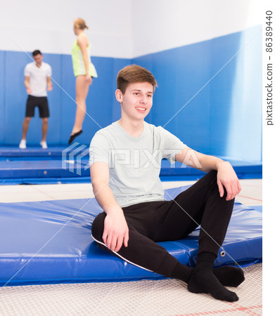 Smiling teenage boy resting on trampoline Smiling teenage boy resting on trampoline 86389440