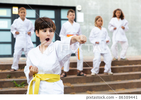 Boy in kimono during training karate exercises at summer outdoors Boy in kimono during training karate exercises at summer outdoors 86389441
