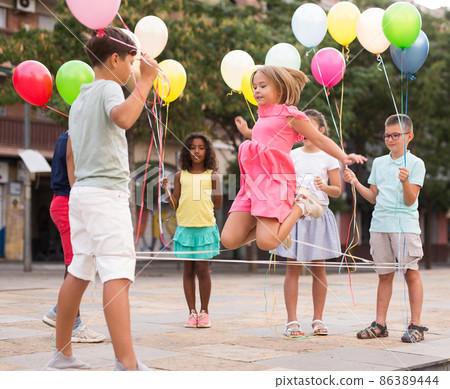Happy tweenagers with balloons playing chinese jump rope in yard Happy tweenagers with balloons playing chinese jump rope in yard 86389444