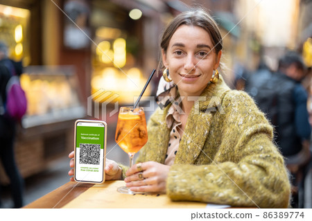 Woman showing green pass while sitting at outdoor bar 86389774