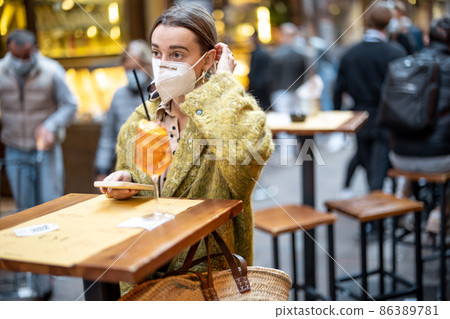 Woman takes off medical mask while sitting at outdoor cafe 86389781