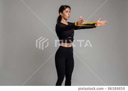 Girl doing arm and shoulder exercises with resistance band on grey background 86389850