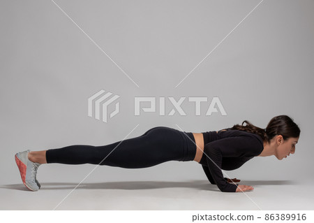 Woman in black sportswear doing push-ups on grey background Woman in black sportswear doing push-ups on grey background 86389916