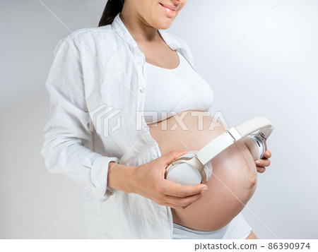 Pregnant woman music lover put the headphones on her belly to let Rebecca enjoy the music she likes. Girl waiting for a baby keeps headphones on her stomach Pregnant woman music lover put the headphones on her belly to let Rebecca enjoy the music she likes. Girl waiting for a baby keeps headphones on her stomach 86390974