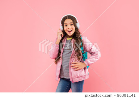 amazed child listen music in headphones and carry backpack on pink background, education amazed child listen music in headphones and carry backpack on pink background, education 86391141