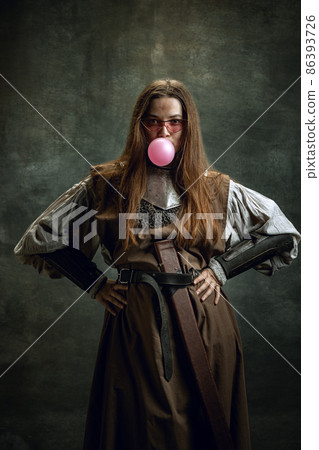 Portrait of adorable woman, medieval female warrior or knight with dirty wounded face looking at camera isolated over dark retro background. Funny meme emotions Portrait of adorable woman, medieval female warrior or knight with dirty wounded face looking at camera isolated over dark retro background. Funny meme emotions 86393726