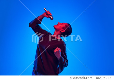 Excited pretty girl, musician and singer with short hair in black sweater singing isolated on dark blue background in neon light. Concept of emotions Excited pretty girl, musician and singer with short hair in black sweater singing isolated on dark blue background in neon light. Concept of emotions 86395222