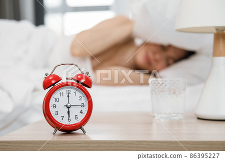 The woman hid under the pillow from the signal of the hated alarm clock. The concept of sleep deprivation and fatigue. The woman hid under the pillow from the signal of the hated alarm clock. The concept of sleep deprivation and fatigue. 86395227