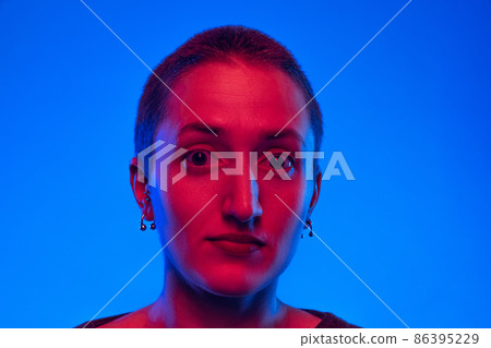 Close-up young shocked woman, student with short hair looking at camera isolated on dark blue background in neon light. Concept of emotions, gender x Close-up young shocked woman, student with short hair looking at camera isolated on dark blue background in neon light. Concept of emotions, gender x 86395229