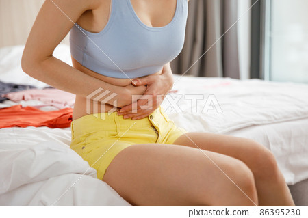 Cystitis in a woman. A young woman has a pain in the lower abdomen, she holds her stomach with her hand. Cystitis in a woman. A young woman has a pain in the lower abdomen, she holds her stomach with her hand. 86395230