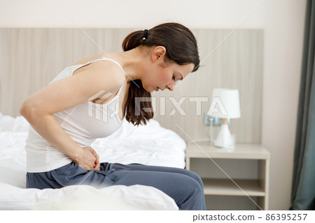 Cystitis in a woman. A young woman has a pain in the lower abdomen, she holds her stomach with her hand. Cystitis in a woman. A young woman has a pain in the lower abdomen, she holds her stomach with her hand. 86395257