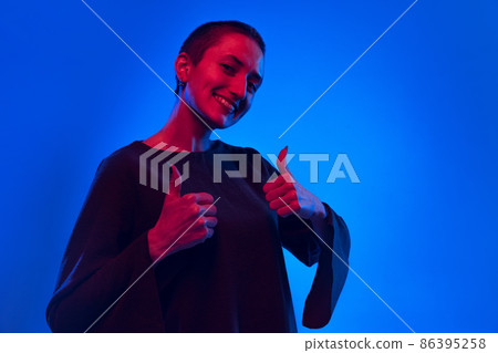 One young happy woman, student with short hair in black sweater gesturing isolated on dark blue background in neon light. Concept of emotions One young happy woman, student with short hair in black sweater gesturing isolated on dark blue background in neon light. Concept of emotions 86395258