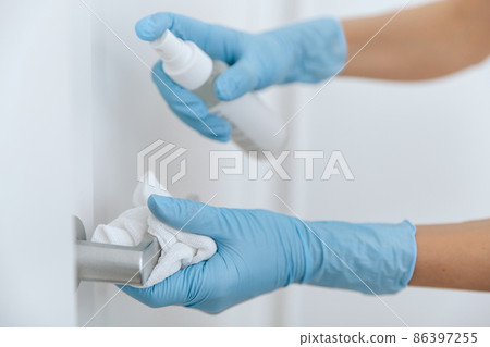 Cleaning black door handle with an antiseptic wet wipe, blue gloves and sanitizer. Woman hand using towel for cleaning. Sanitize surfaces prevention in hospital and public spaces against corona virus. Cleaning black door handle with an antiseptic wet wipe, blue gloves and sanitizer. Woman hand using towel for cleaning. Sanitize surfaces prevention in hospital and public spaces against corona virus. 86397255