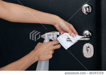 Cleaning black door handles with an antiseptic wet wipe. Woman hand using towel for cleaning home room door link. Sanitize surfaces prevention in hospital and public spaces against corona virus. 86397259