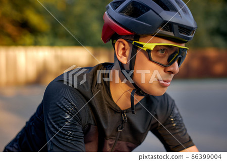 Fit cyclist in black helmet, protective glasses and active wear dynamically riding bicycle Fit cyclist in black helmet, protective glasses and active wear dynamically riding bicycle 86399004