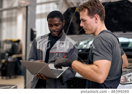 Team Of Diverse Auto Mechanic And Repairman Checking Diagnostics Results on Laptop. 86399269
