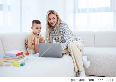 Happy young mother with little kid sit on sofa in living room have fun using laptop 86399944