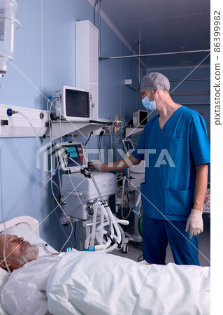 male nurse standing by medical equipment, checking the heartbeat of senior patient 86399982