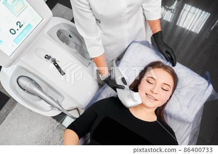 Top view of smiling attractive young woman at reception beautician in clinic. Concept of process procedure for improvements face skin with special modern machine or equipments for care. Top view of smiling attractive young woman at reception beautician in clinic. Concept of process procedure for improvements face skin with special modern machine or equipments for care. 86400733