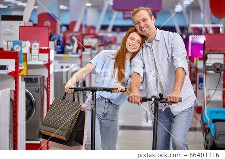 Portrait of happy caucasian man and woman on electric kick scooters shopping 86401116