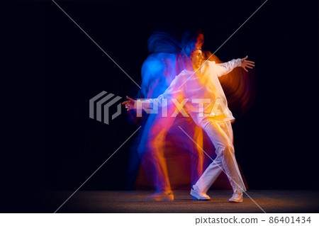 Youth dances. Dynamic portrait of hip-hop dancer in action, motion isolated on dark background in mixed neon light. Youth culture, hip-hop, style and fashion 86401434