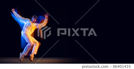 Dynamic portrait of male hip-hop dancer dancing isolated on dark background in mixed neon light. Youth culture, hip-hop, movement, style and fashion, action. 86401435