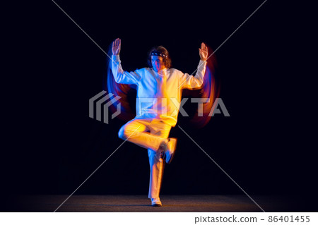 Stylish man in sports white suit dancing hip-hop isolated on dark background in mixed neon light. Youth culture, hip-hop, movement, style and fashion, action. 86401455