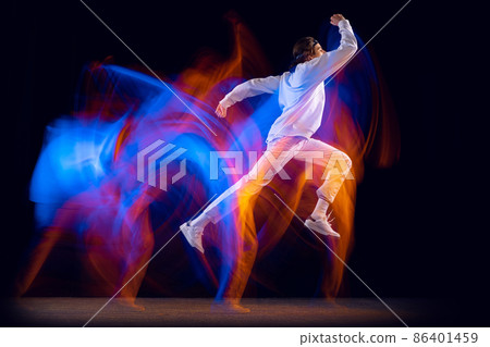 Flexible man in sports white suit dancing hip-hop isolated on dark background in mixed neon light. Youth culture, hip-hop, movement, style and fashion, action. Flexible man in sports white suit dancing hip-hop isolated on dark background in mixed neon light. Youth culture, hip-hop, movement, style and fashion, action. 86401459